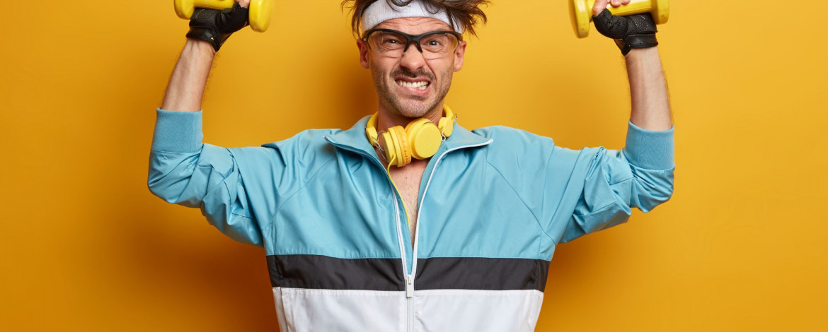 Junger Mann mit einer hellblauen Trainingsjacke, zwei gelben Trainingshanteln in der Hand, sowie gelben Kopfhörern um den Nacken steht als Symbol für Empowerment in der IT.